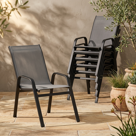 Grey textilene outdoor dining chair beside a stack of matching chairs in a warm sandstone courtyard